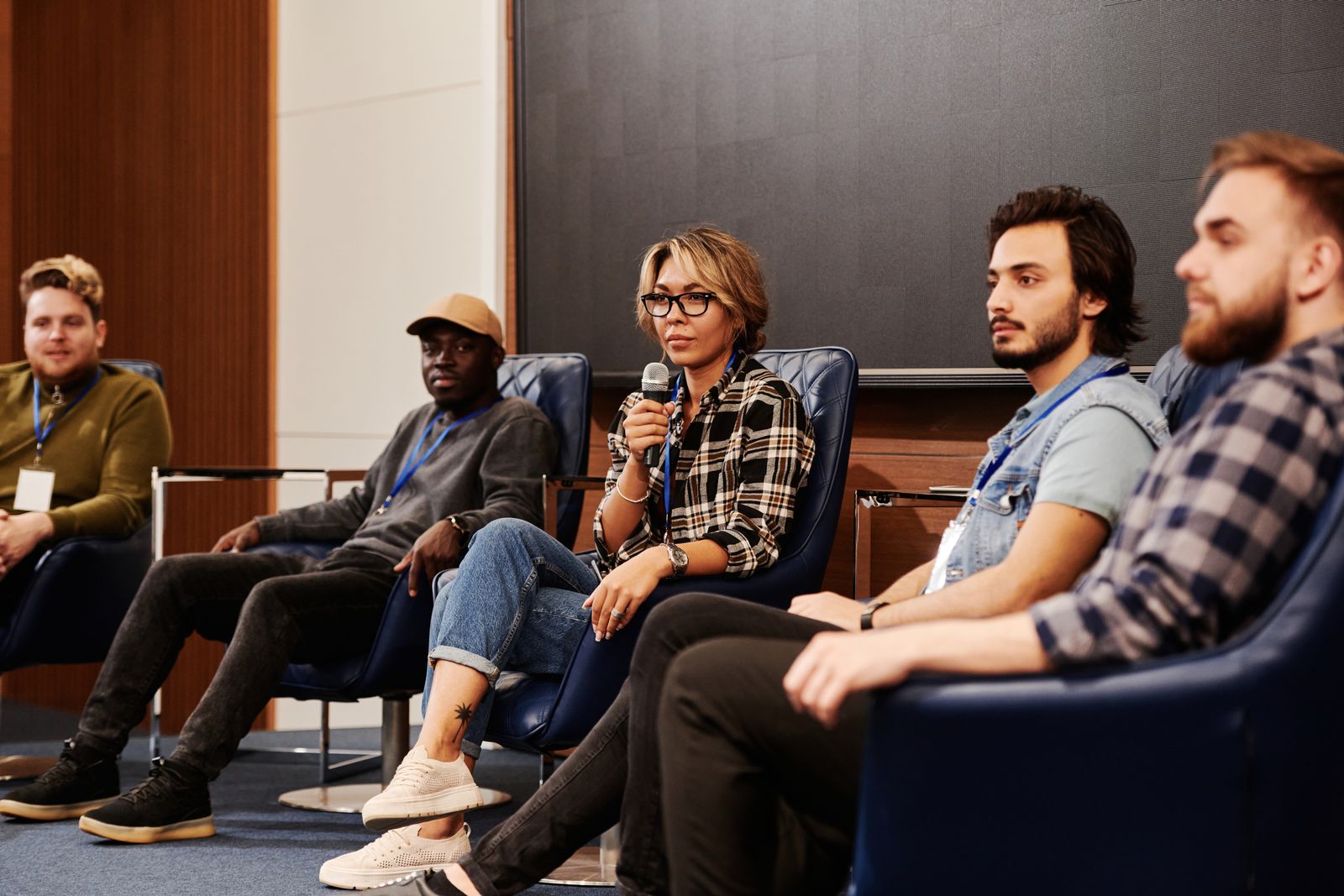 A woman holding a microphone during a seated panel discussion with four other adults.