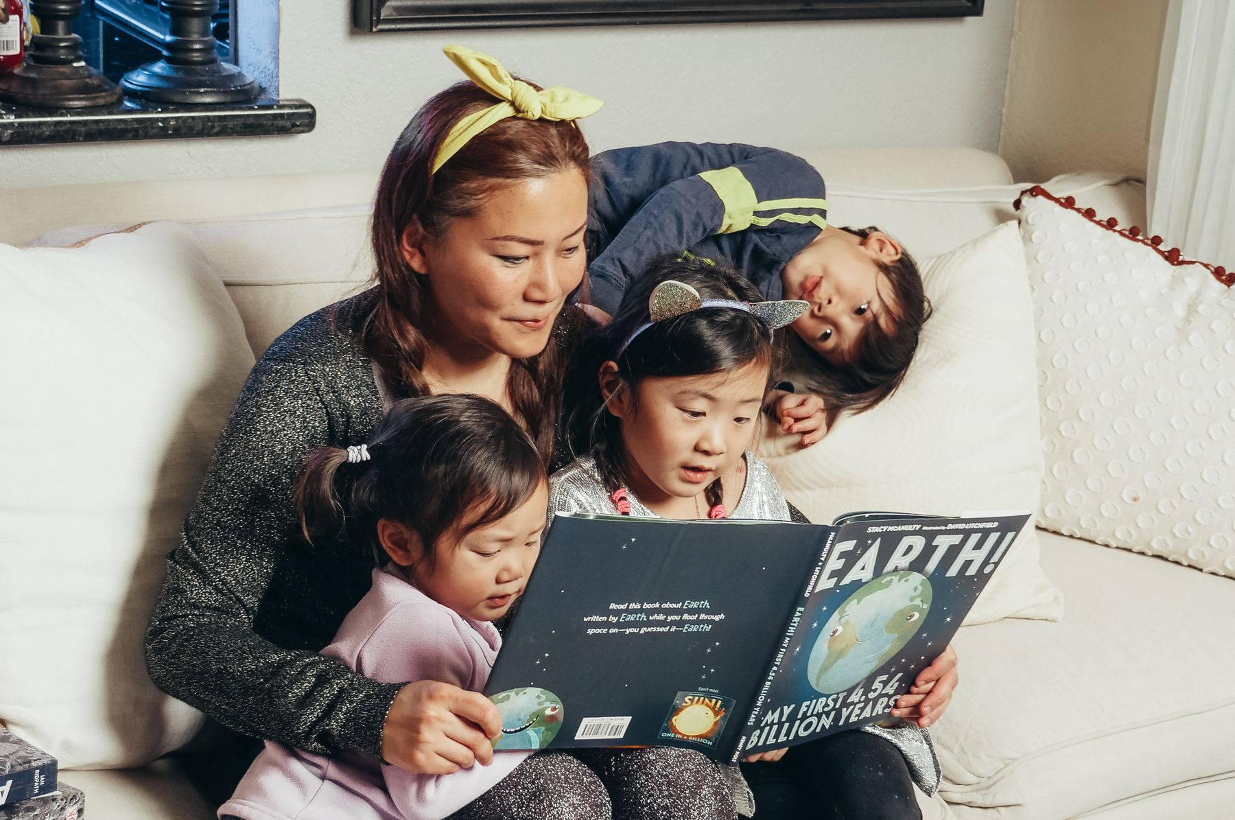 A mother and three children reading a book together on a sofa.